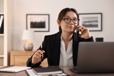 Photo of Beautiful businesswoman talking on smartphone at table in office