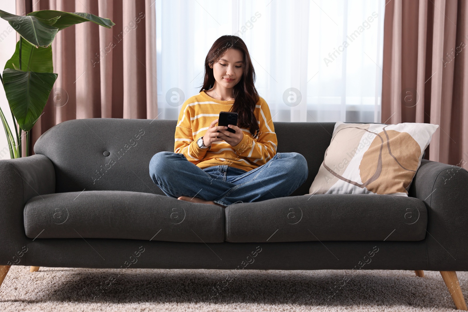 Photo of Beautiful woman using smartphone on sofa at home