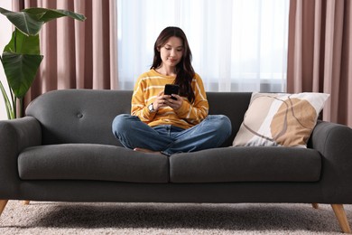 Photo of Beautiful woman using smartphone on sofa at home