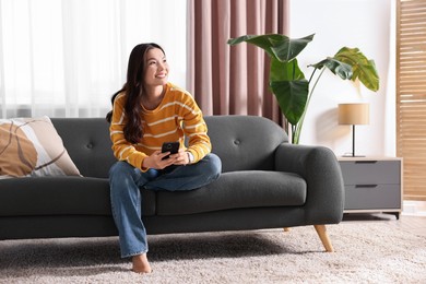 Photo of Smiling woman with smartphone on sofa at home