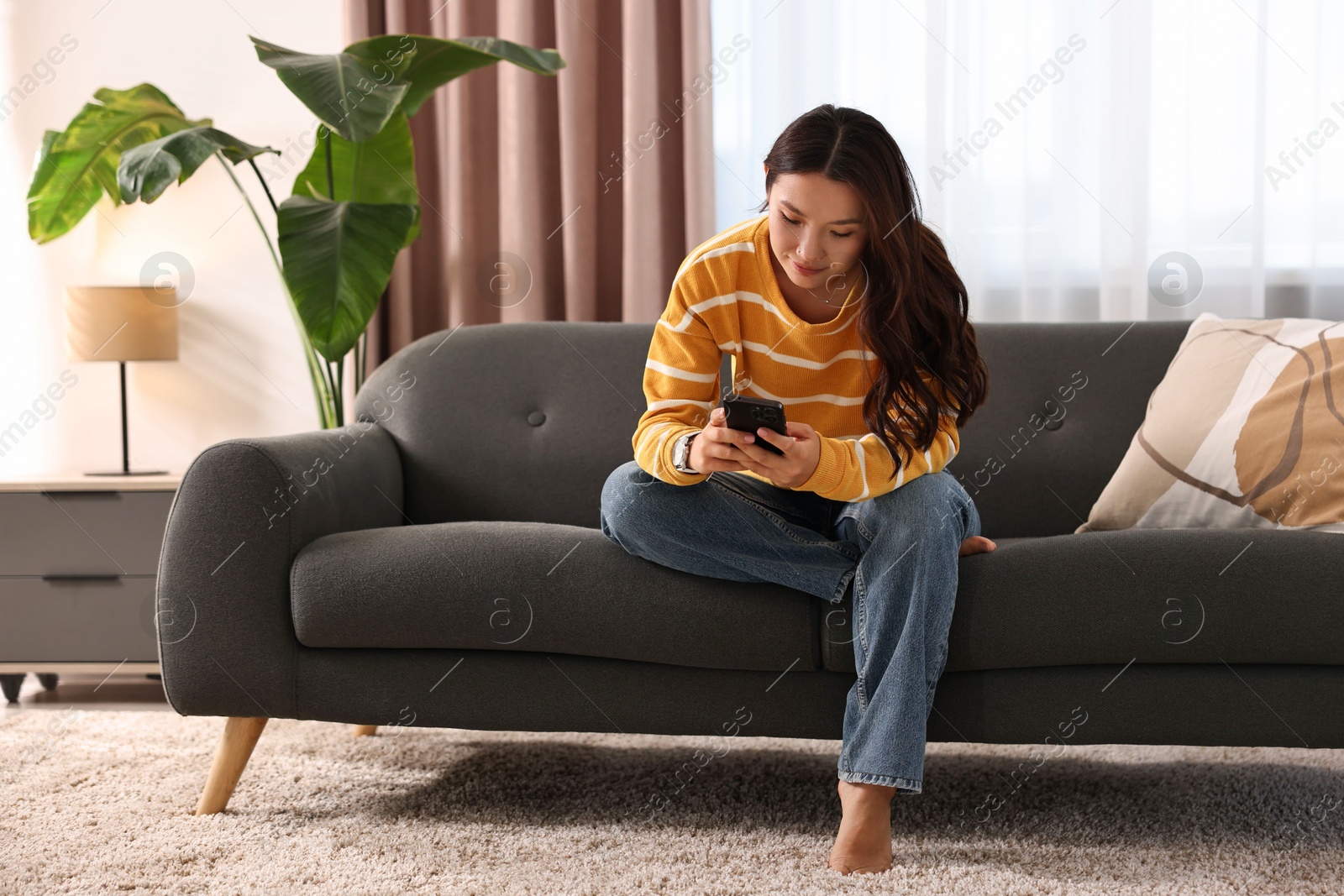 Photo of Beautiful woman using smartphone on sofa at home