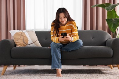 Beautiful woman using smartphone on sofa at home