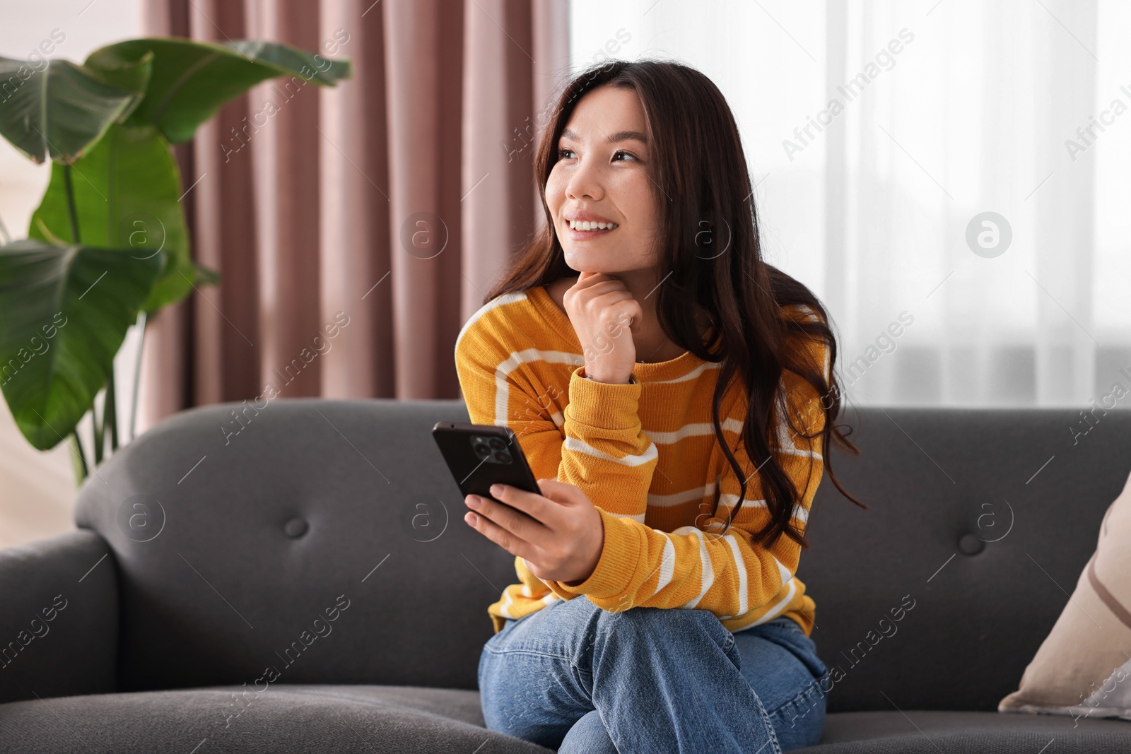 Photo of Smiling woman with smartphone on sofa at home