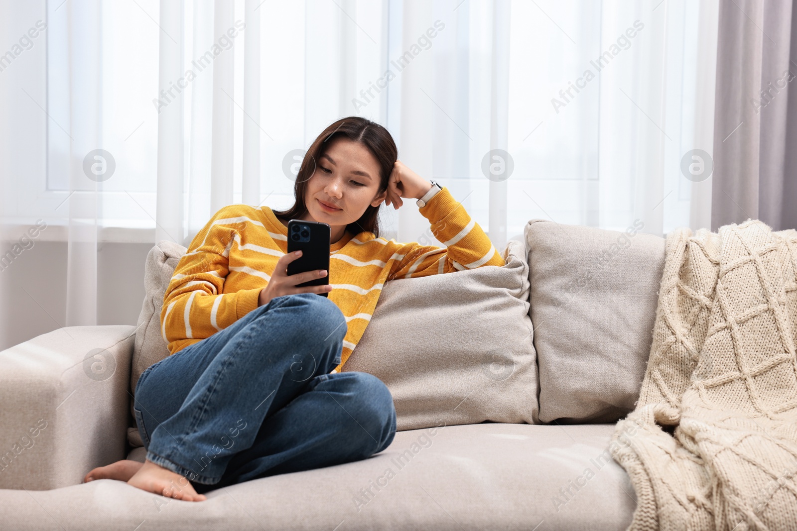 Photo of Beautiful woman using smartphone on sofa at home