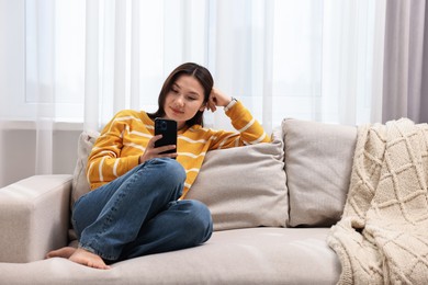 Photo of Beautiful woman using smartphone on sofa at home