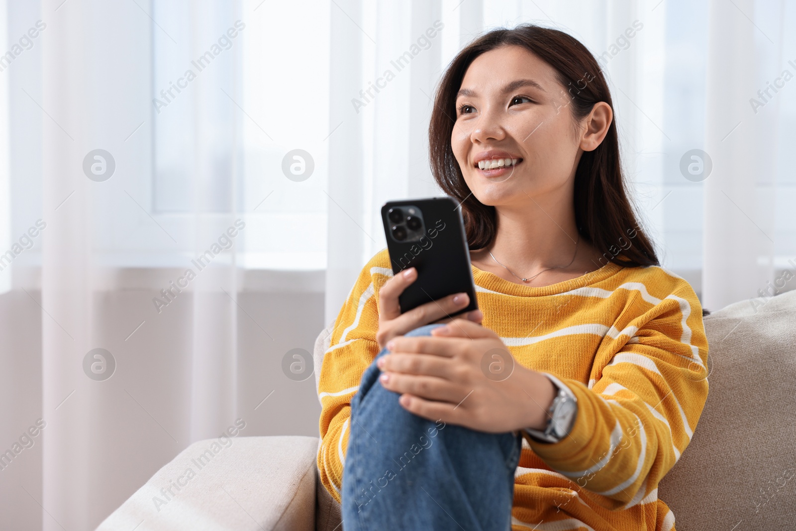 Photo of Smiling woman with smartphone at home. Space for text