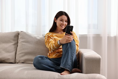 Photo of Smiling woman using smartphone on sofa at home