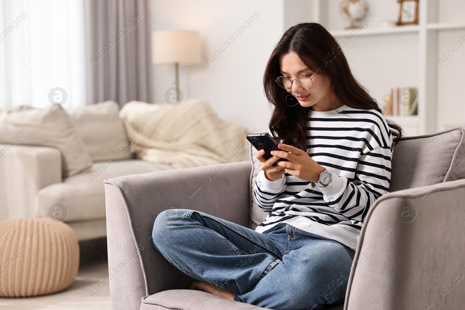 Photo of Beautiful woman with smartphone on armchair at home