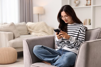 Beautiful woman with smartphone on armchair at home