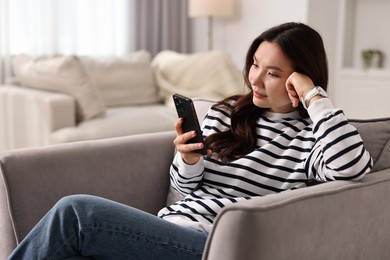 Beautiful woman with smartphone on armchair at home