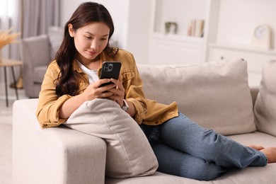 Beautiful woman with smartphone on sofa at home