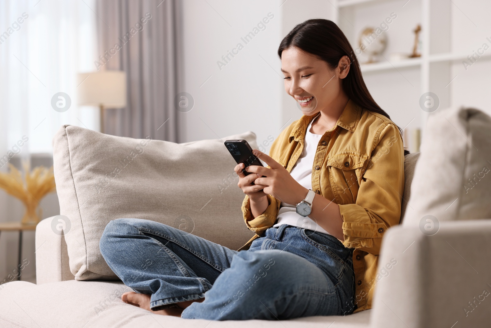 Photo of Smiling woman with smartphone on sofa at home