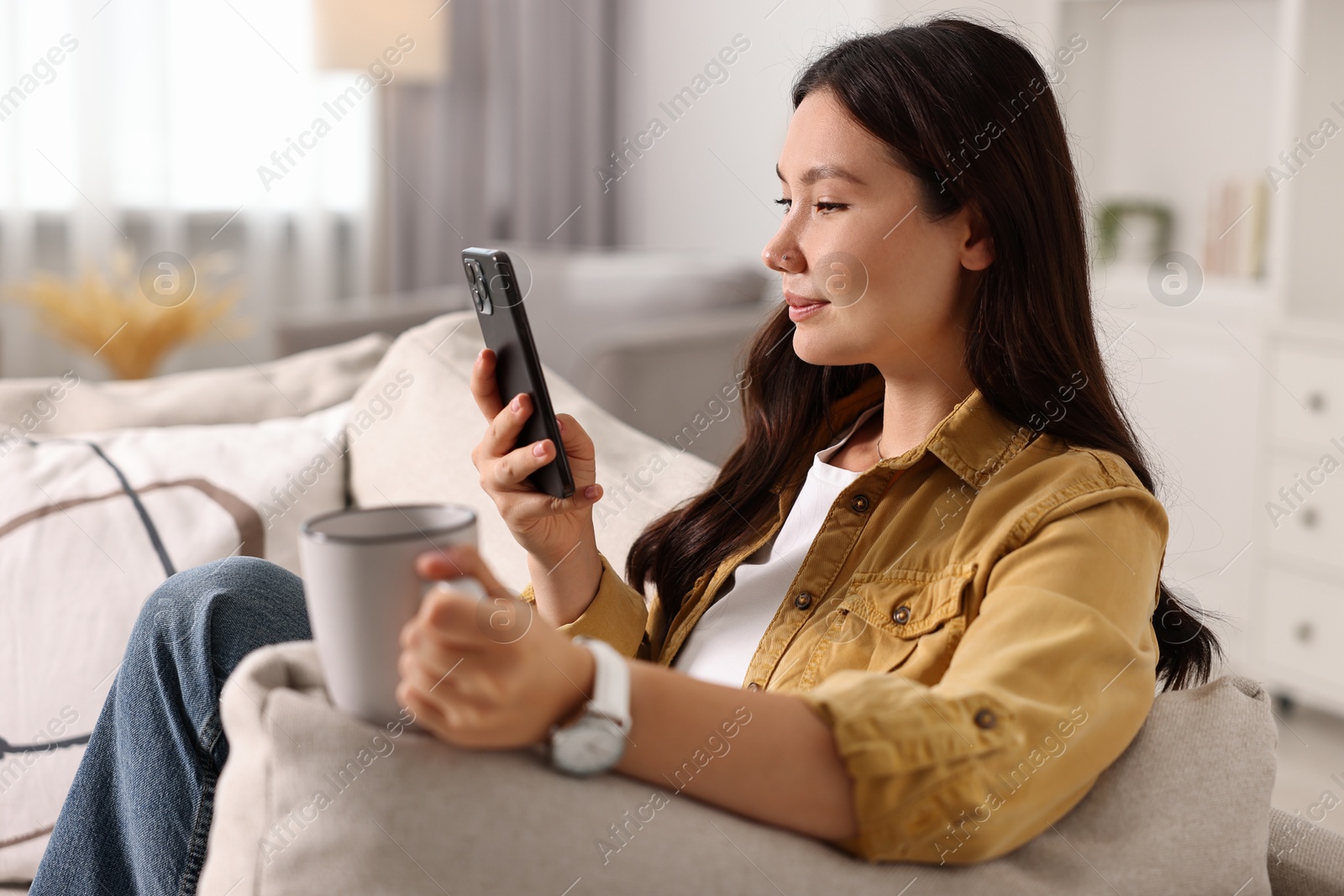 Photo of Beautiful woman with smartphone and cup on sofa at home