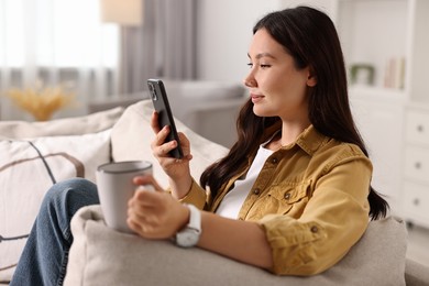 Photo of Beautiful woman with smartphone and cup on sofa at home