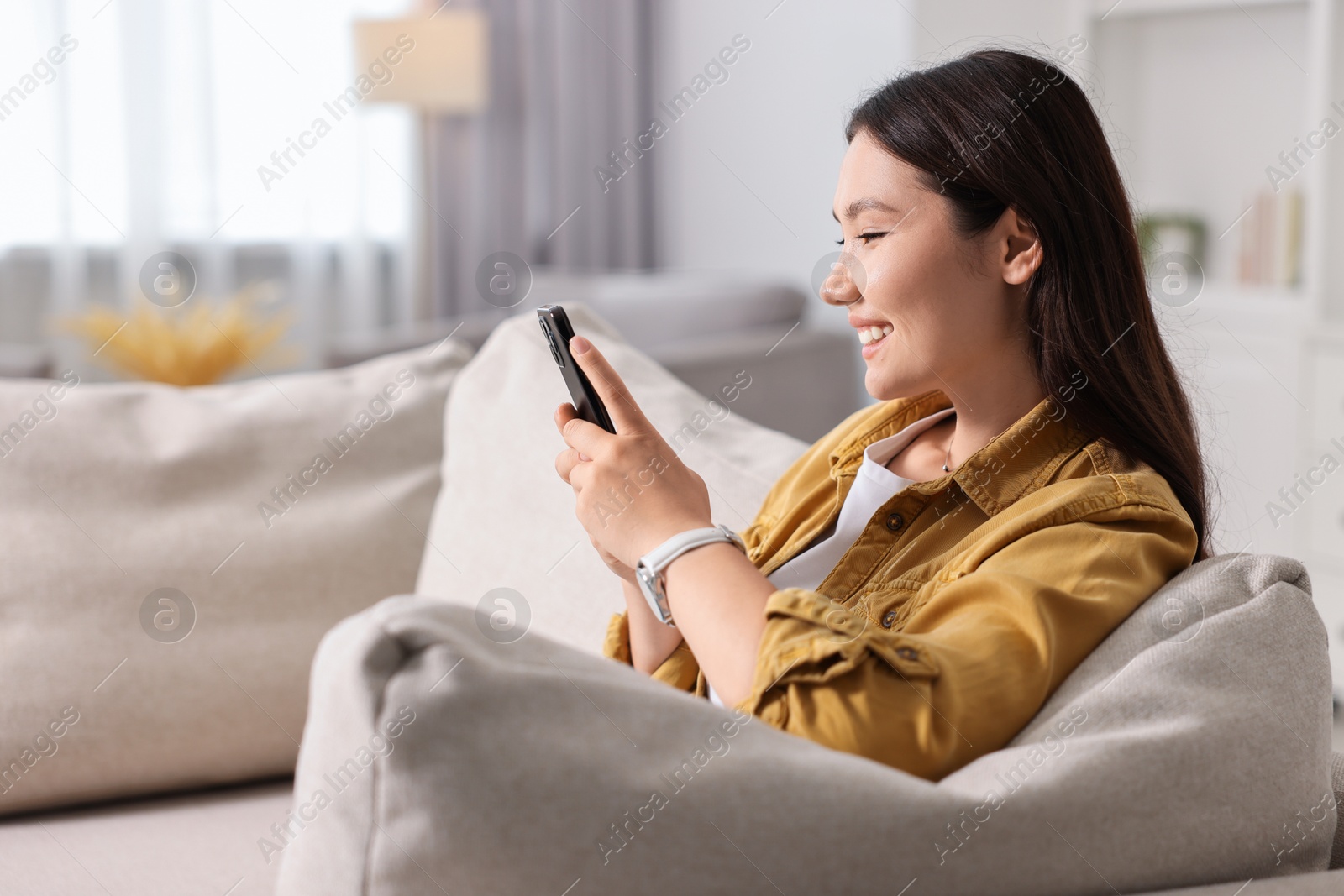 Photo of Smiling woman with smartphone on sofa at home