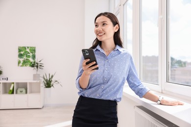 Photo of Smiling businesswoman with smartphone in office. Space for text