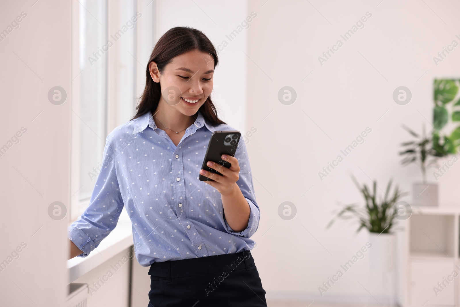 Photo of Smiling businesswoman using smartphone in office. Space for text