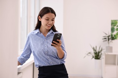 Photo of Smiling businesswoman using smartphone in office. Space for text