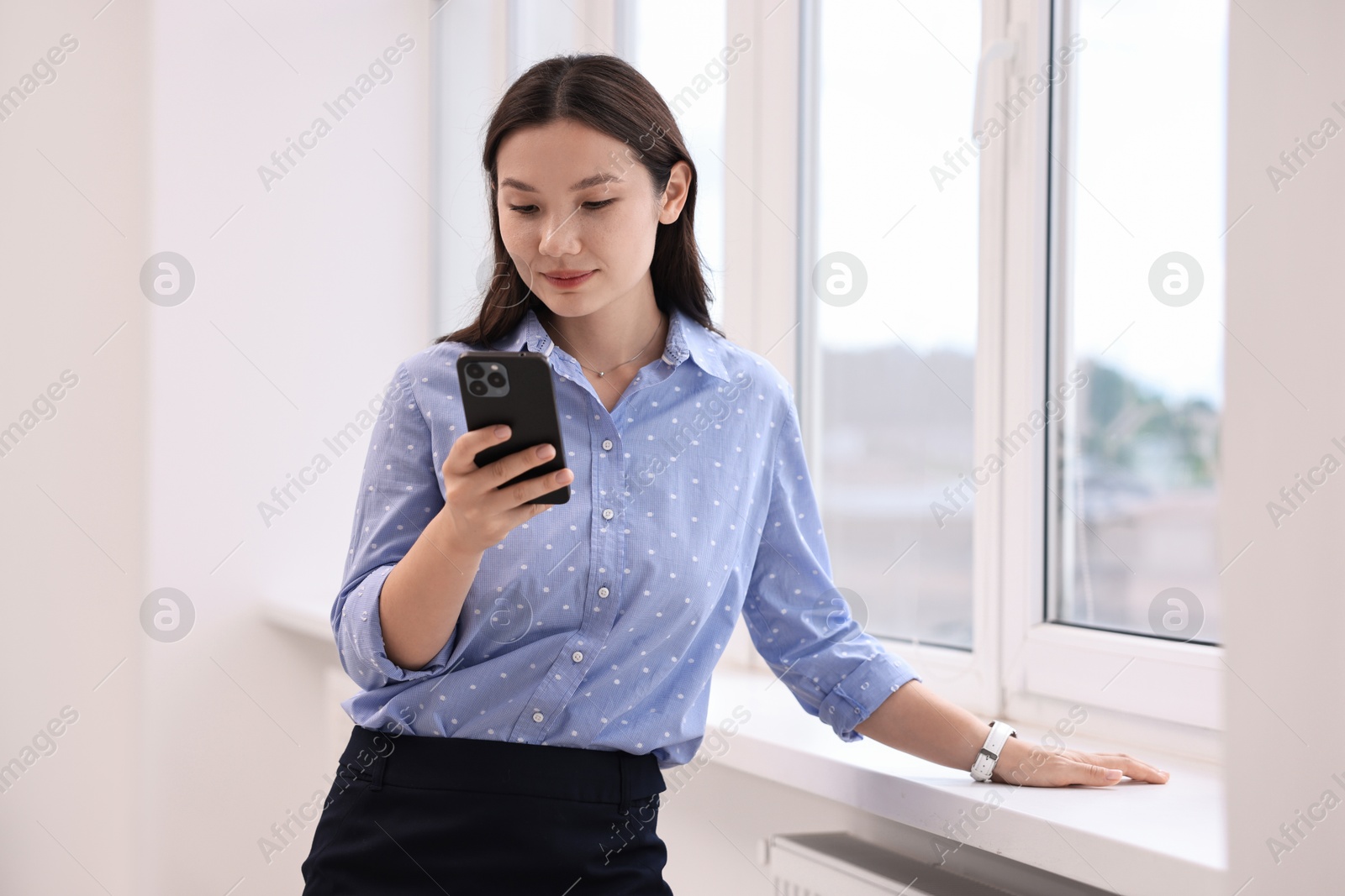 Photo of Beautiful businesswoman with smartphone near window in office