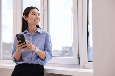 Smiling businesswoman with smartphone in office. Space for text