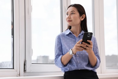 Beautiful businesswoman with smartphone in office. Space for text