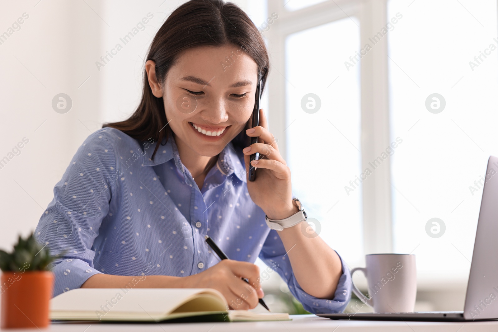 Photo of Smiling businesswoman talking on smartphone at table in office