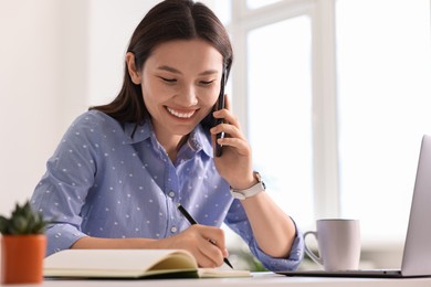 Photo of Smiling businesswoman talking on smartphone at table in office