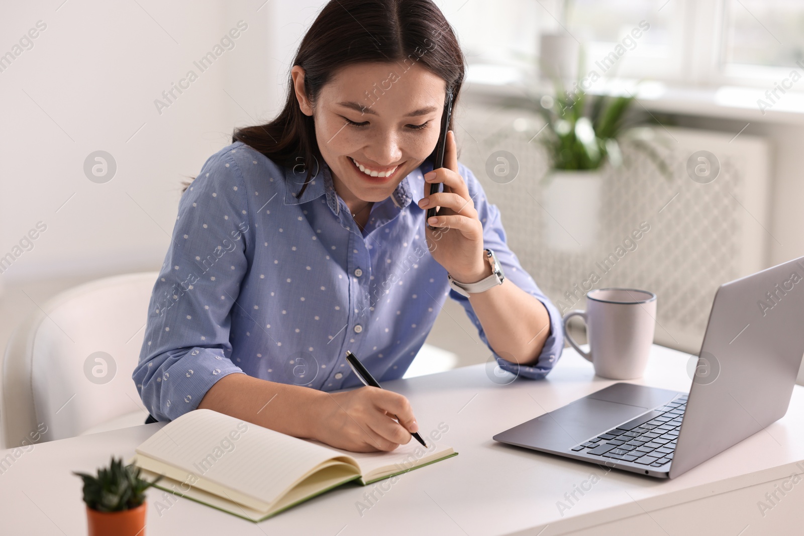 Photo of Smiling businesswoman talking on smartphone at table in office