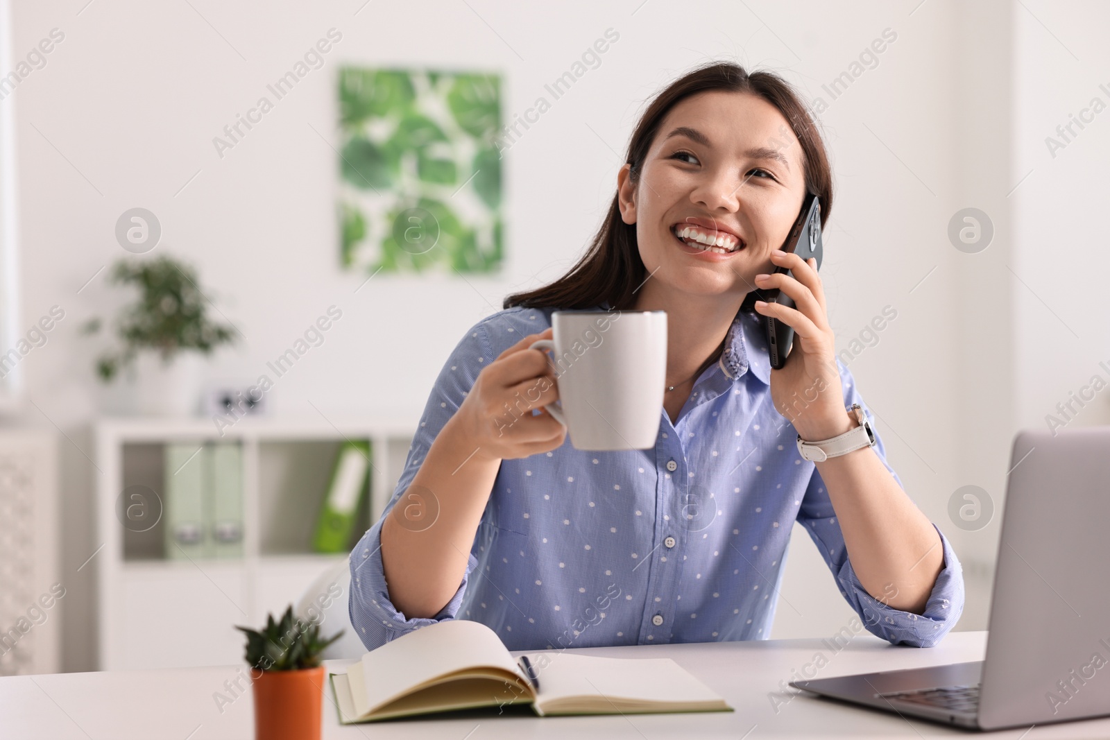 Photo of Smiling businesswoman talking on smartphone at table in office