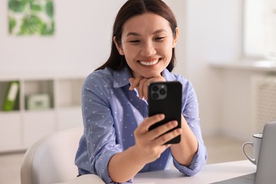 Photo of Smiling businesswoman with smartphone at table in office