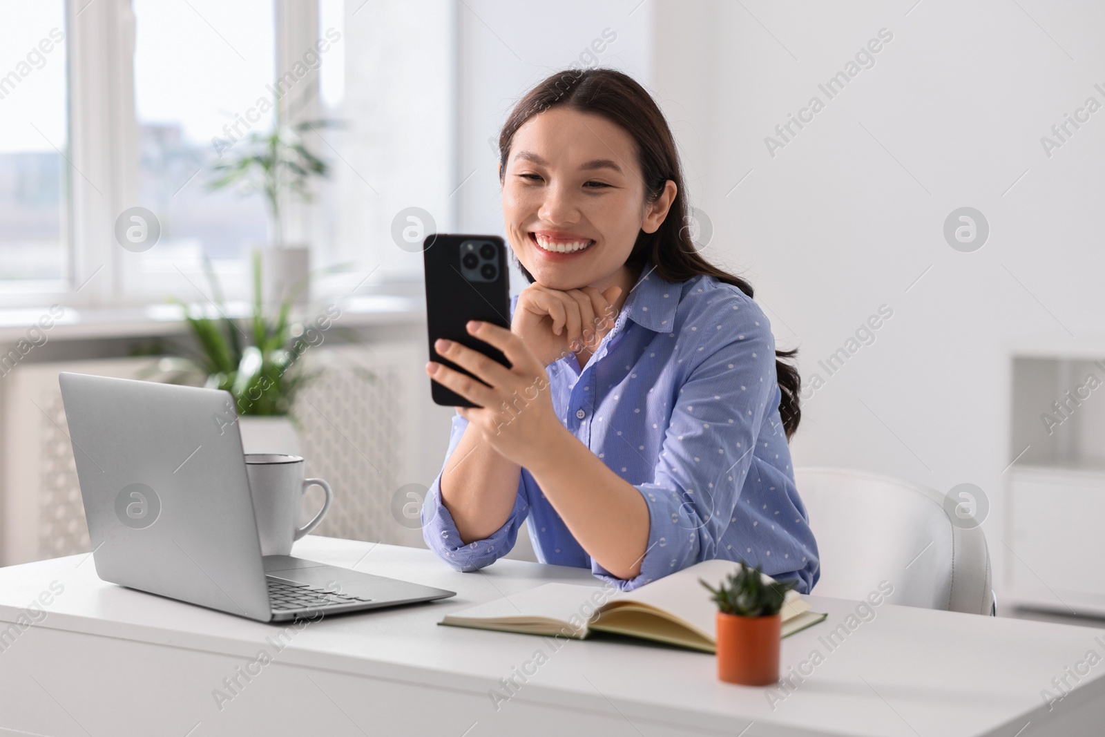 Photo of Smiling businesswoman with smartphone at table in office