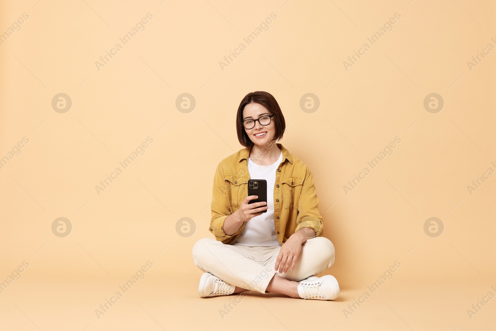 Photo of Smiling woman with smartphone sitting on beige background