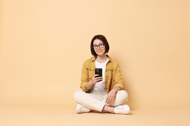 Smiling woman with smartphone sitting on beige background