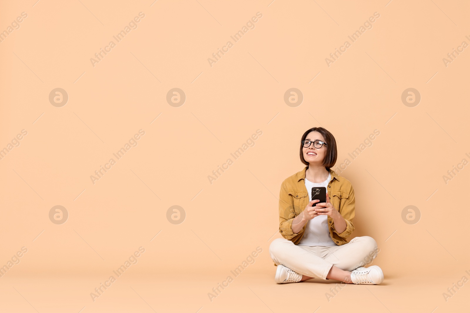 Photo of Smiling woman with smartphone sitting on beige background. Space for text