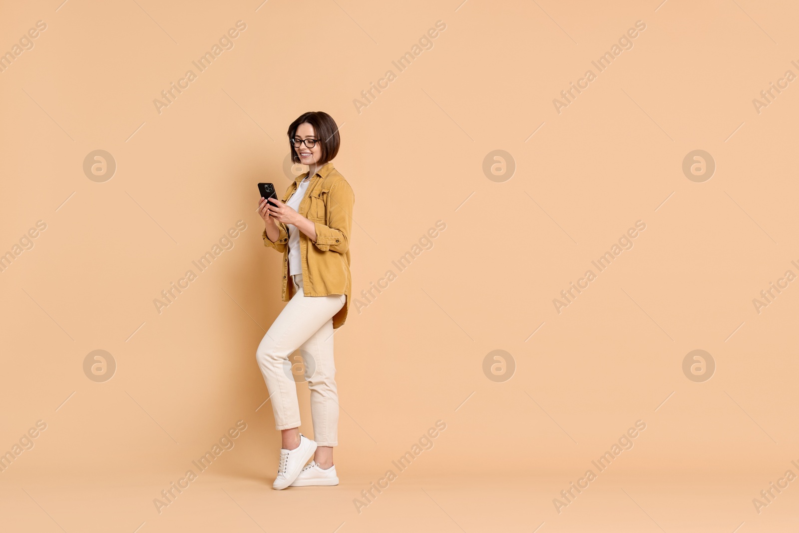 Photo of Smiling woman with smartphone on beige background. Space for text