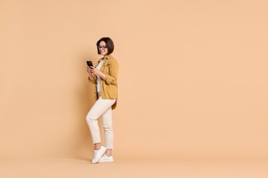 Smiling woman with smartphone on beige background. Space for text