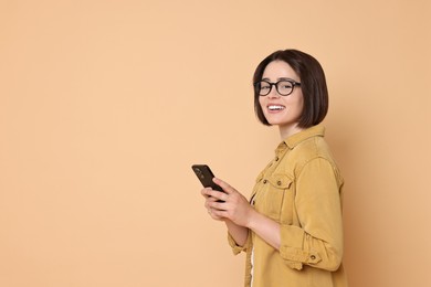 Smiling woman with smartphone on beige background. Space for text