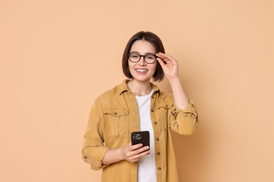 Smiling woman with smartphone on beige background