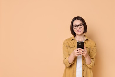 Smiling woman with smartphone on beige background. Space for text