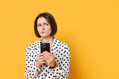 Photo of Portrait of thoughtful woman with smartphone on yellow background. Space for text