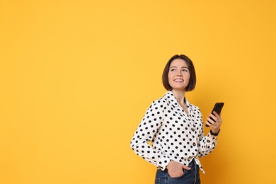 Smiling woman with smartphone on yellow background. Space for text