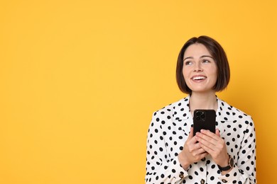 Smiling woman with smartphone on yellow background. Space for text