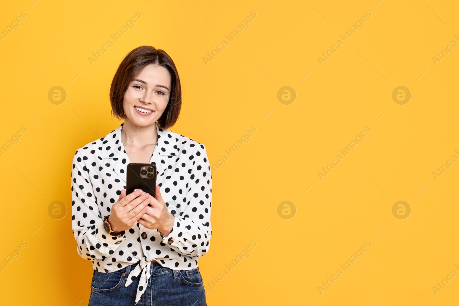 Photo of Smiling woman with smartphone on yellow background. Space for text