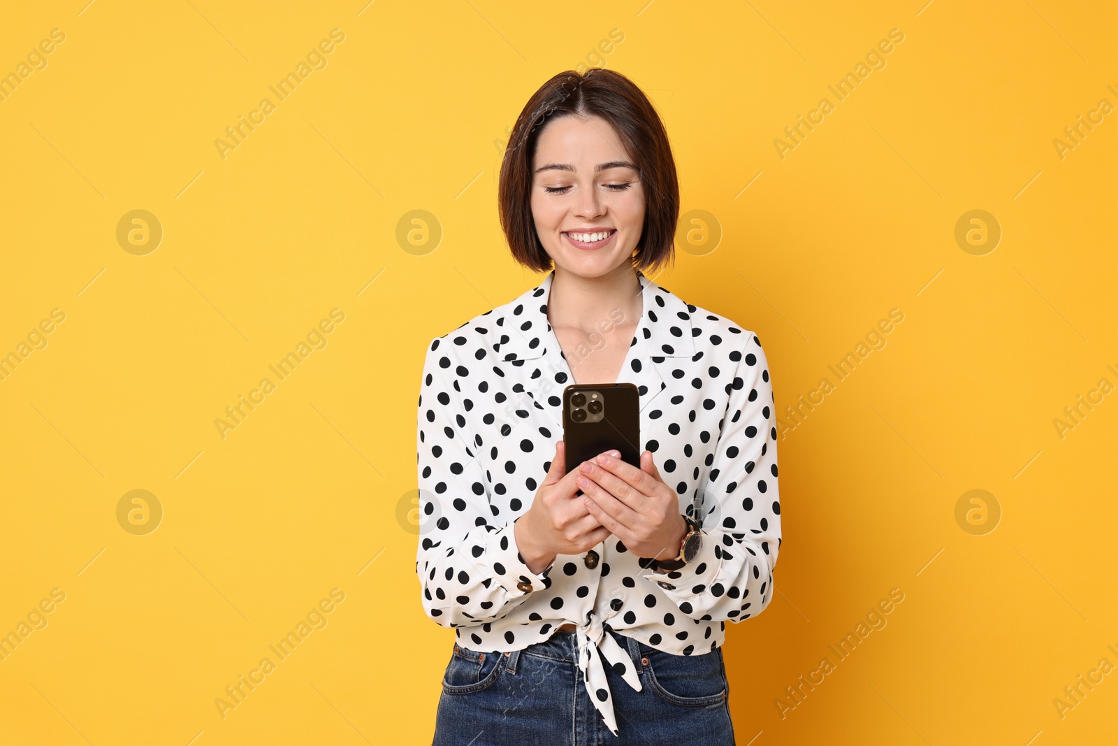 Photo of Smiling woman with smartphone on yellow background