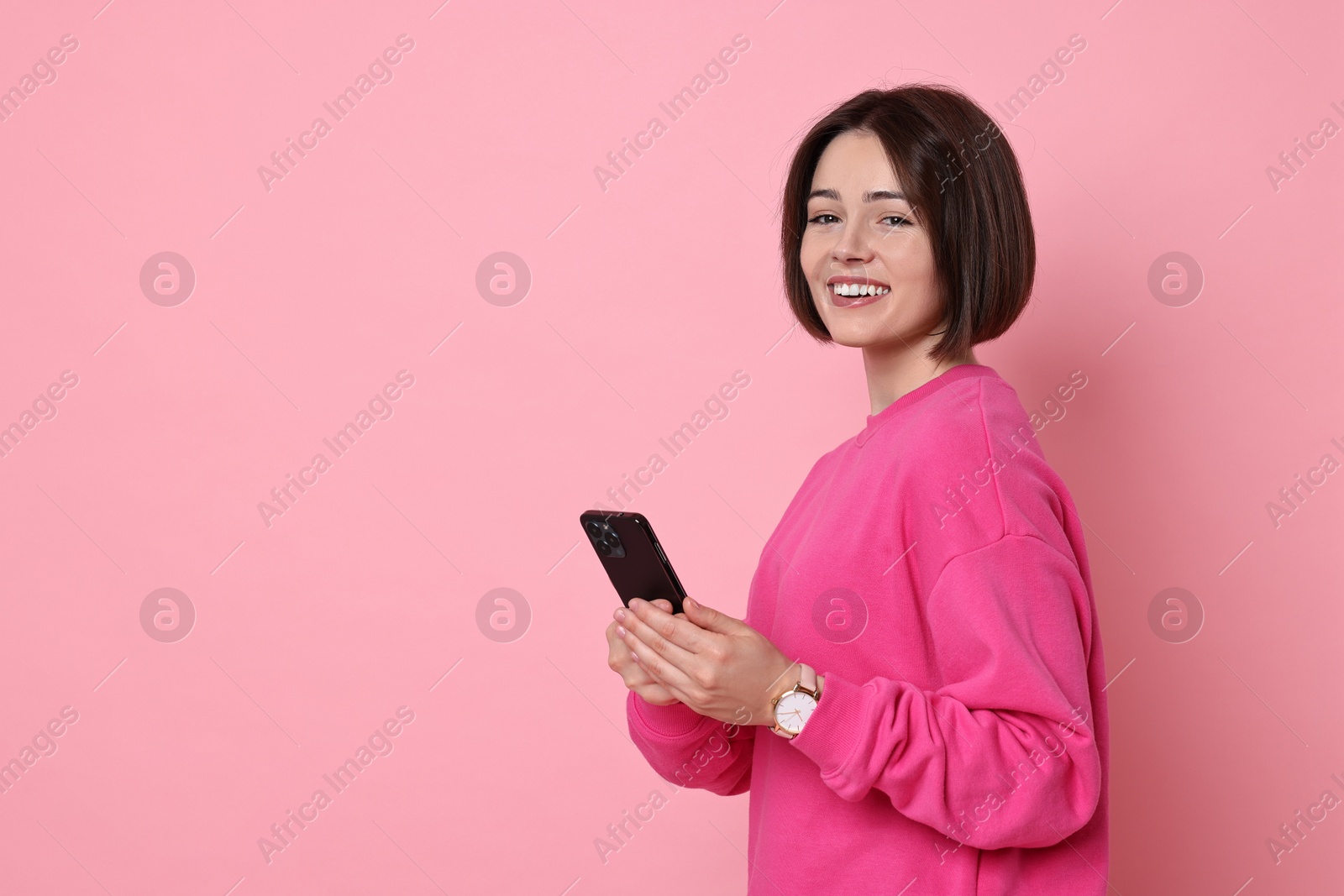 Photo of Smiling woman with smartphone on pink background. Space for text