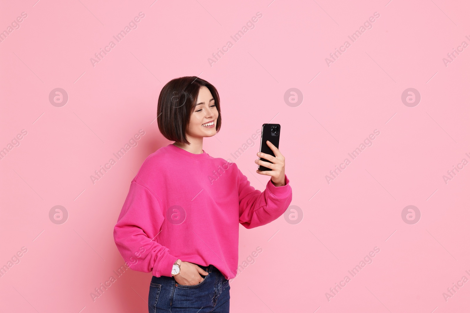 Photo of Smiling woman with smartphone on pink background