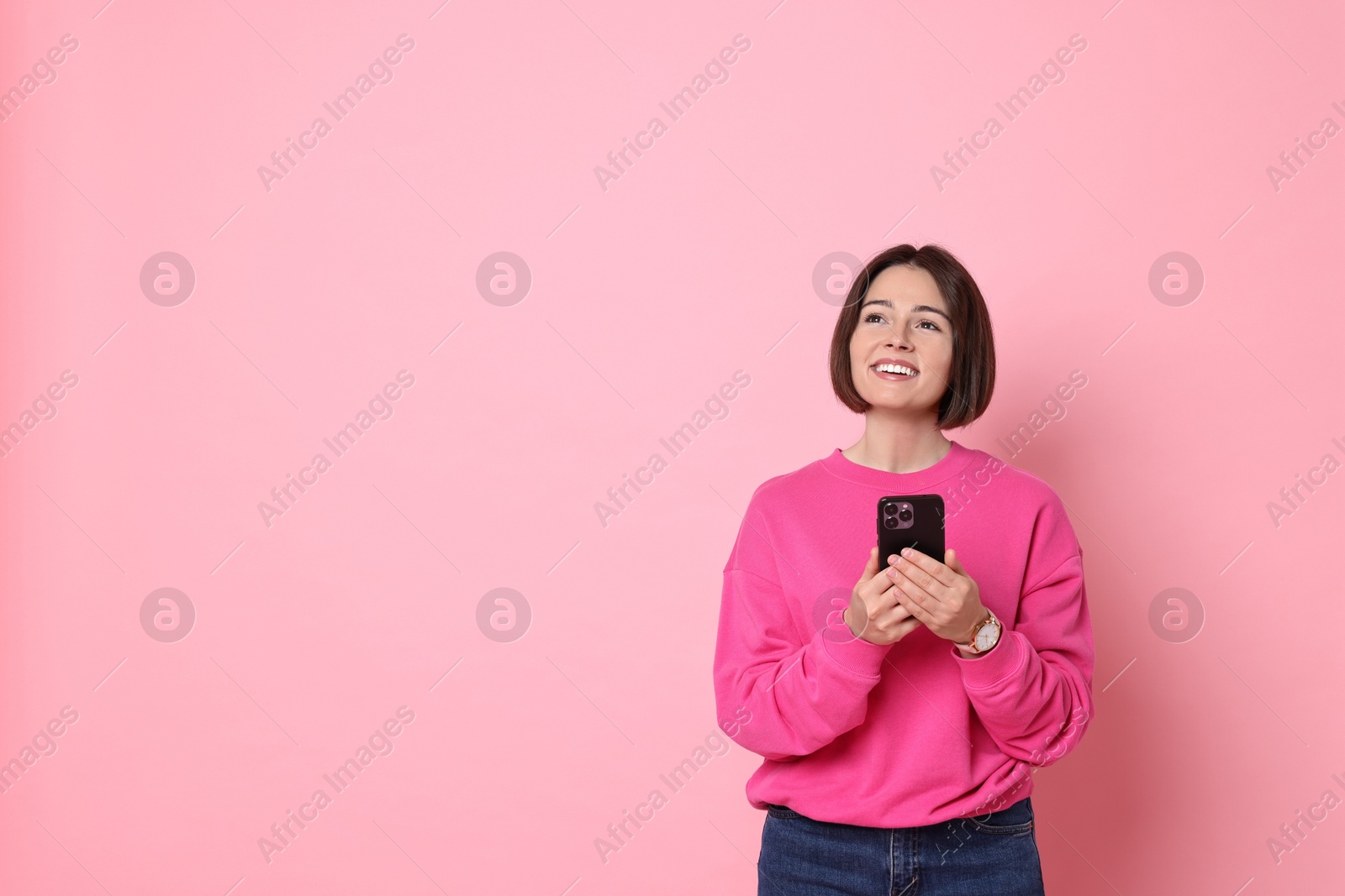 Photo of Smiling woman with smartphone on pink background. Space for text