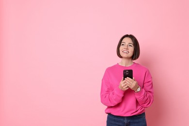 Smiling woman with smartphone on pink background. Space for text