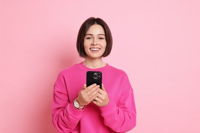 Smiling woman with smartphone on pink background