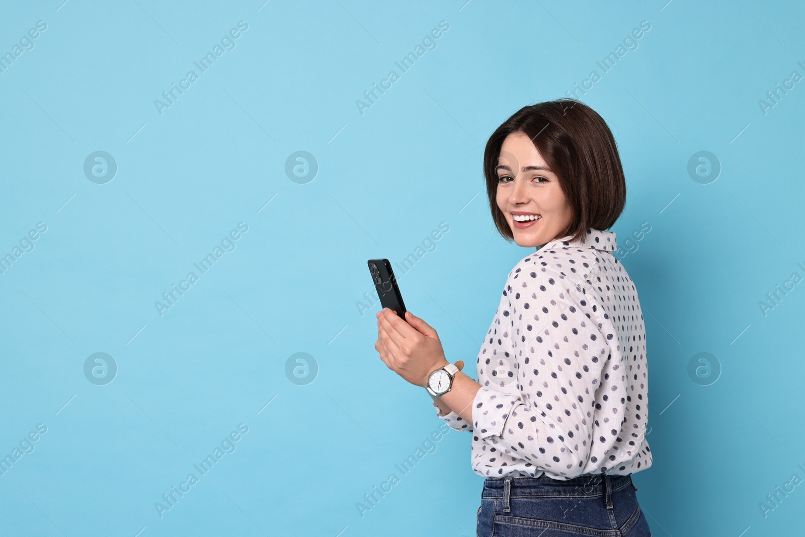 Photo of Smiling woman with smartphone on light blue background. Space for text